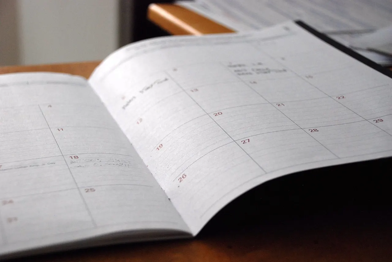 An open monthly planner with dates and handwritten notes on a wooden desk