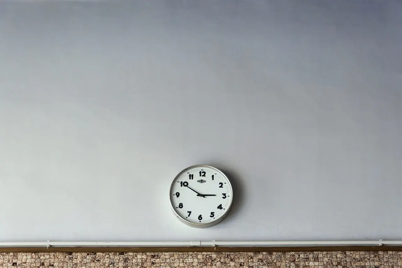 A round white wall clock on a plain pale wall